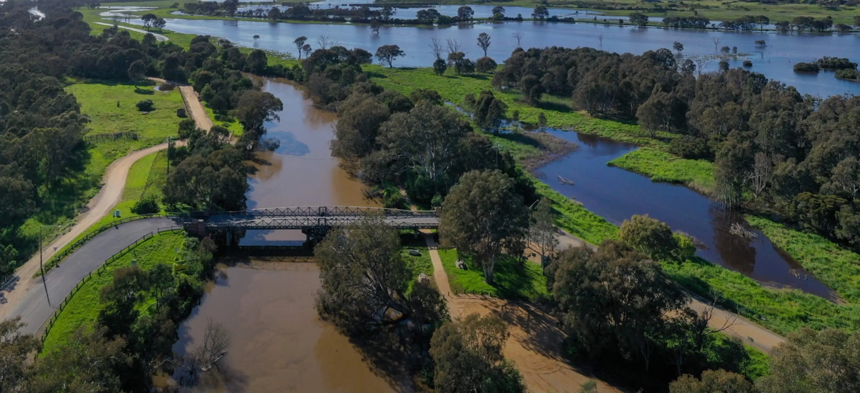 A drone image of an Australian wetland with a bridge traversing a river tributary with the larger river in the background.